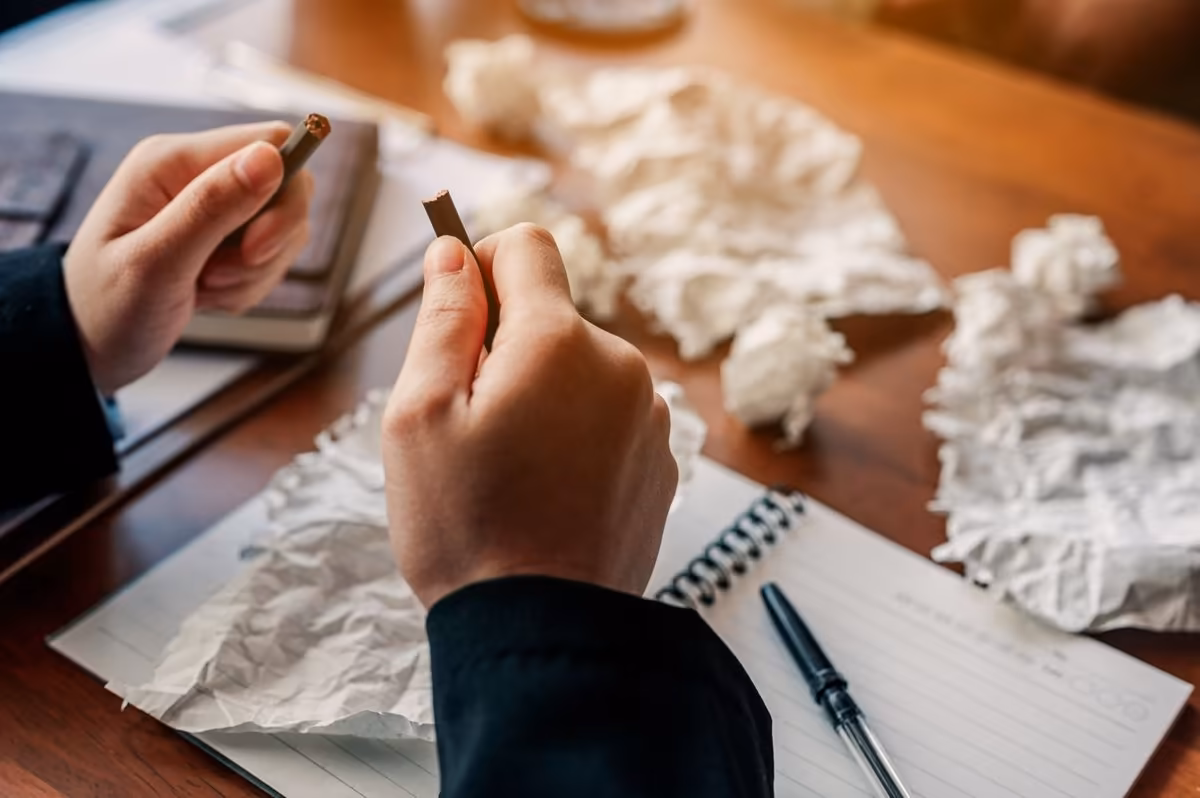 Frustrated writer with discarded drafts, scene reviewed by Qreative