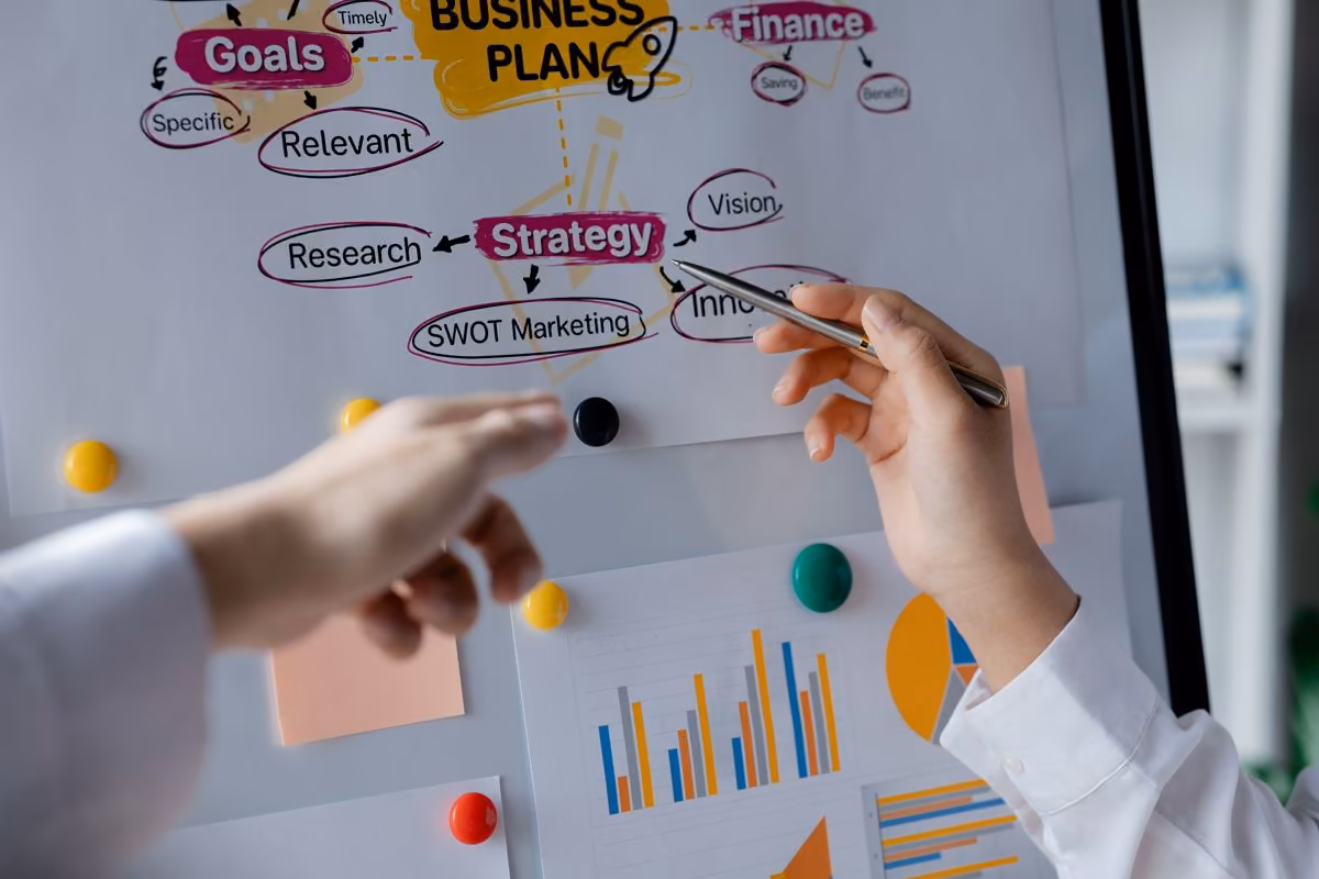 Two hands point to an annotated business plan, discussed by Qreative